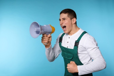 Portrait of emotional male worker using megaphone on color background