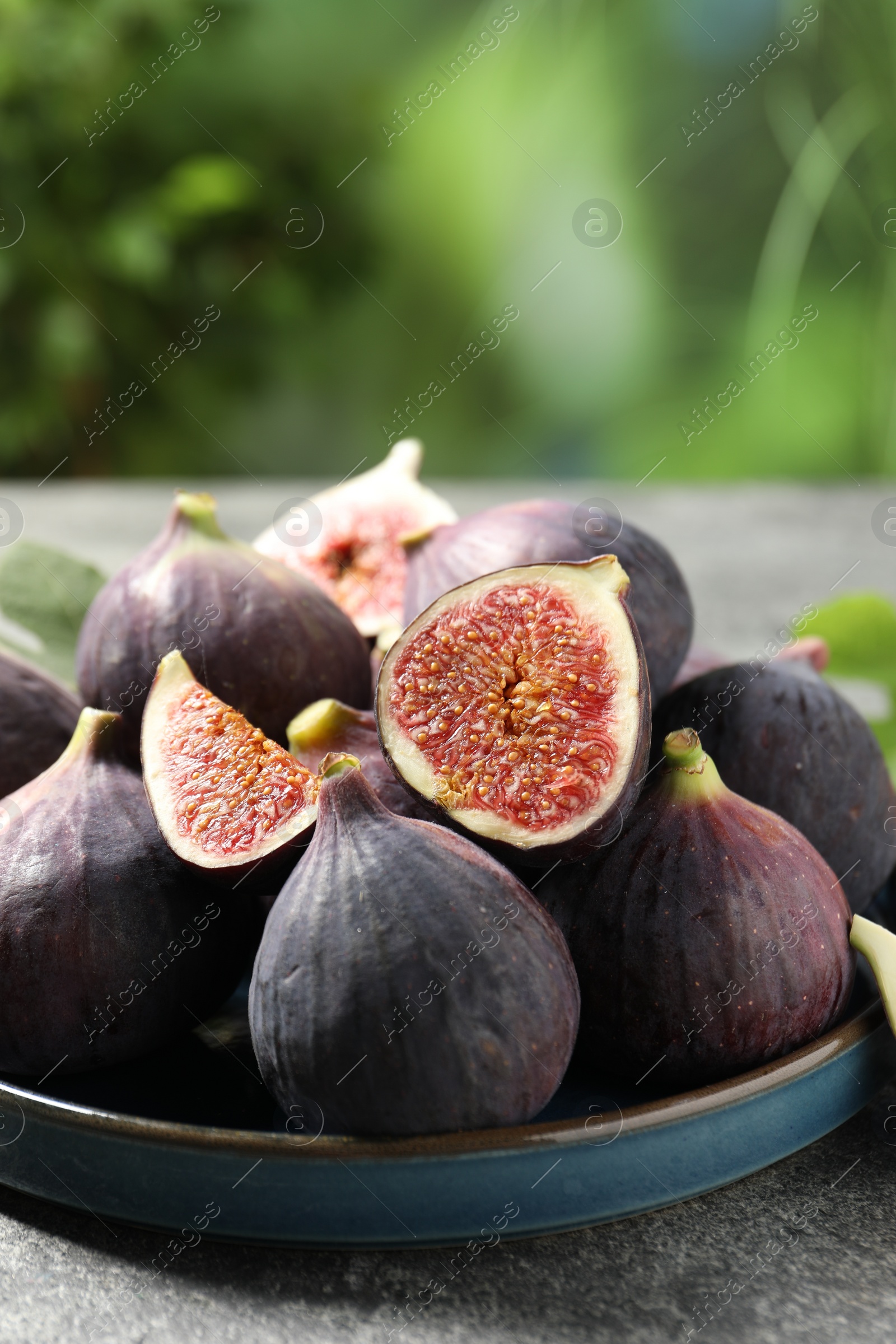 Photo of Whole and cut ripe figs on light grey textured table against blurred green background, closeup