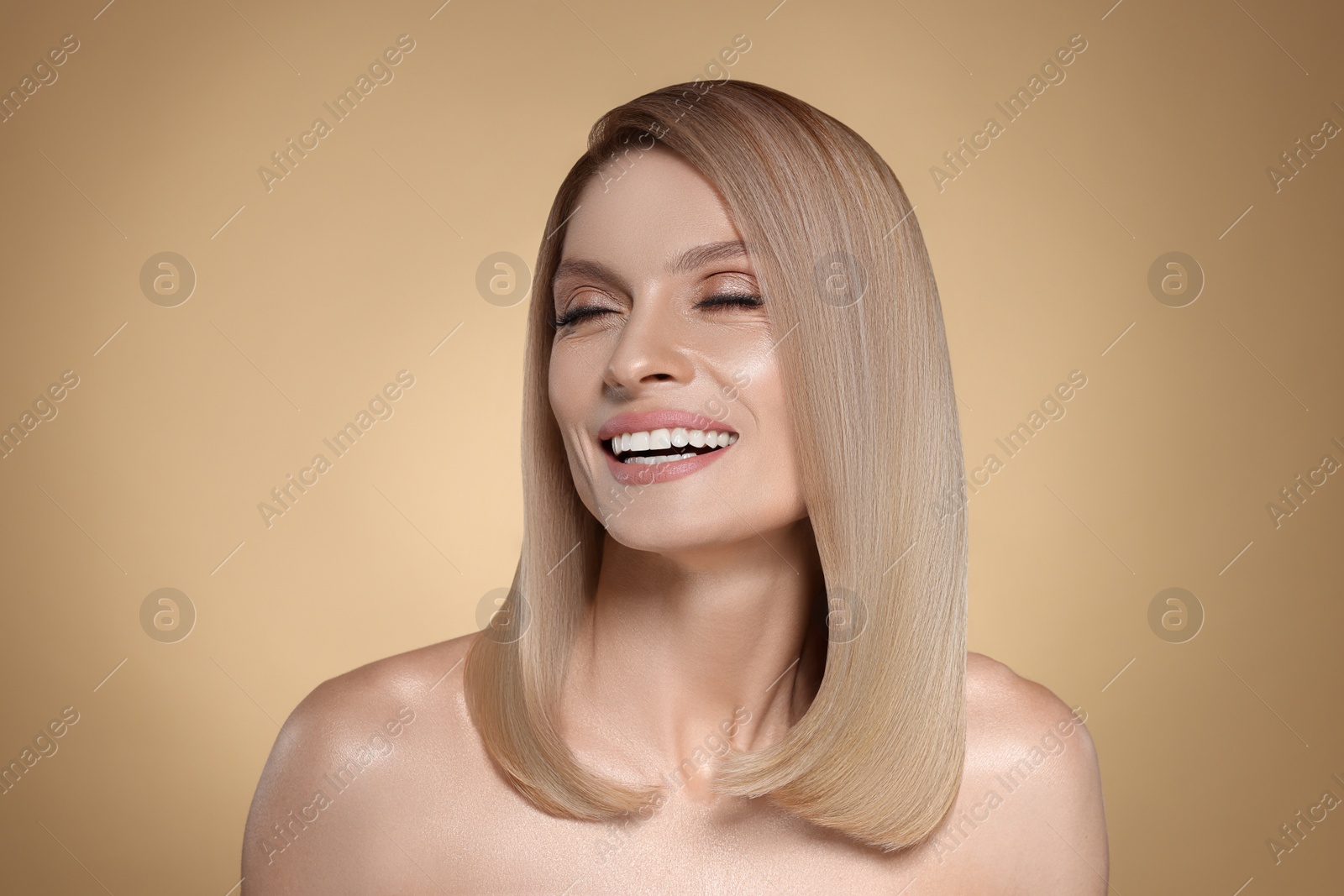 Image of Portrait of attractive woman with blonde hair smiling on dark beige background