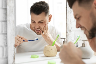 Photo of Young man suffering from toothache in bathroom