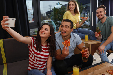 Photo of Happy young people with delicious pizza taking selfie in cafe