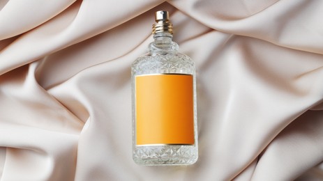 Luxury bottle of perfume on beige silk, top view