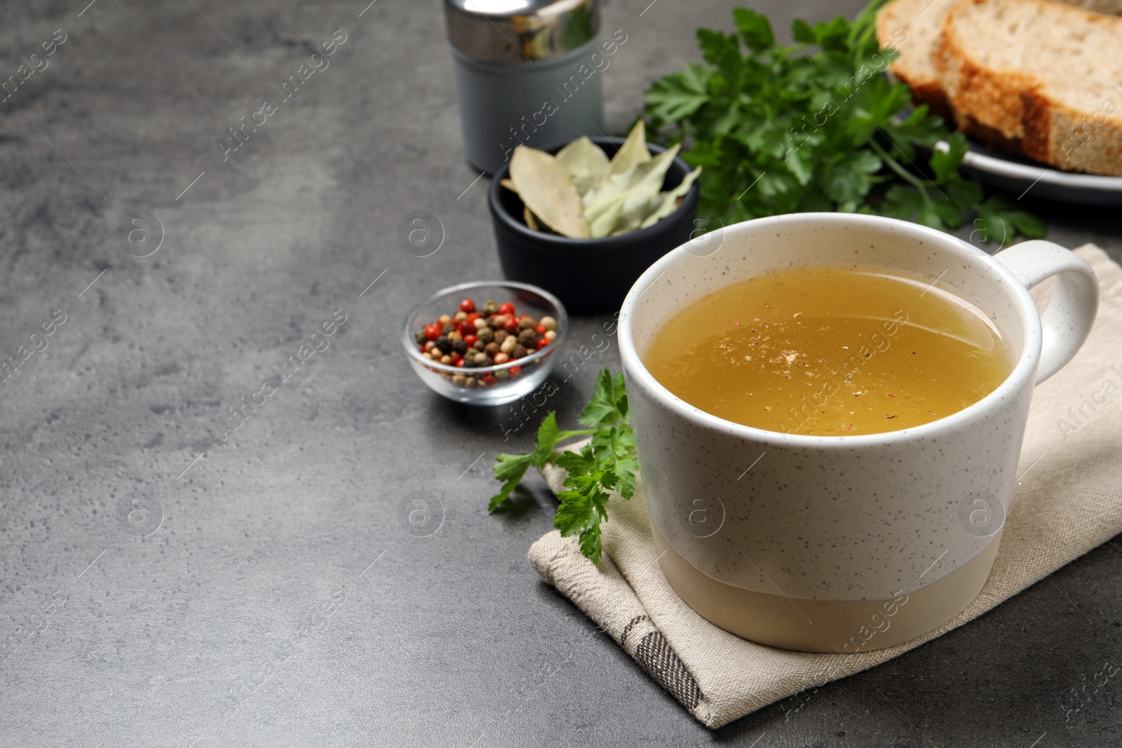 Photo of Hot delicious bouillon in cup on grey table. Space for text