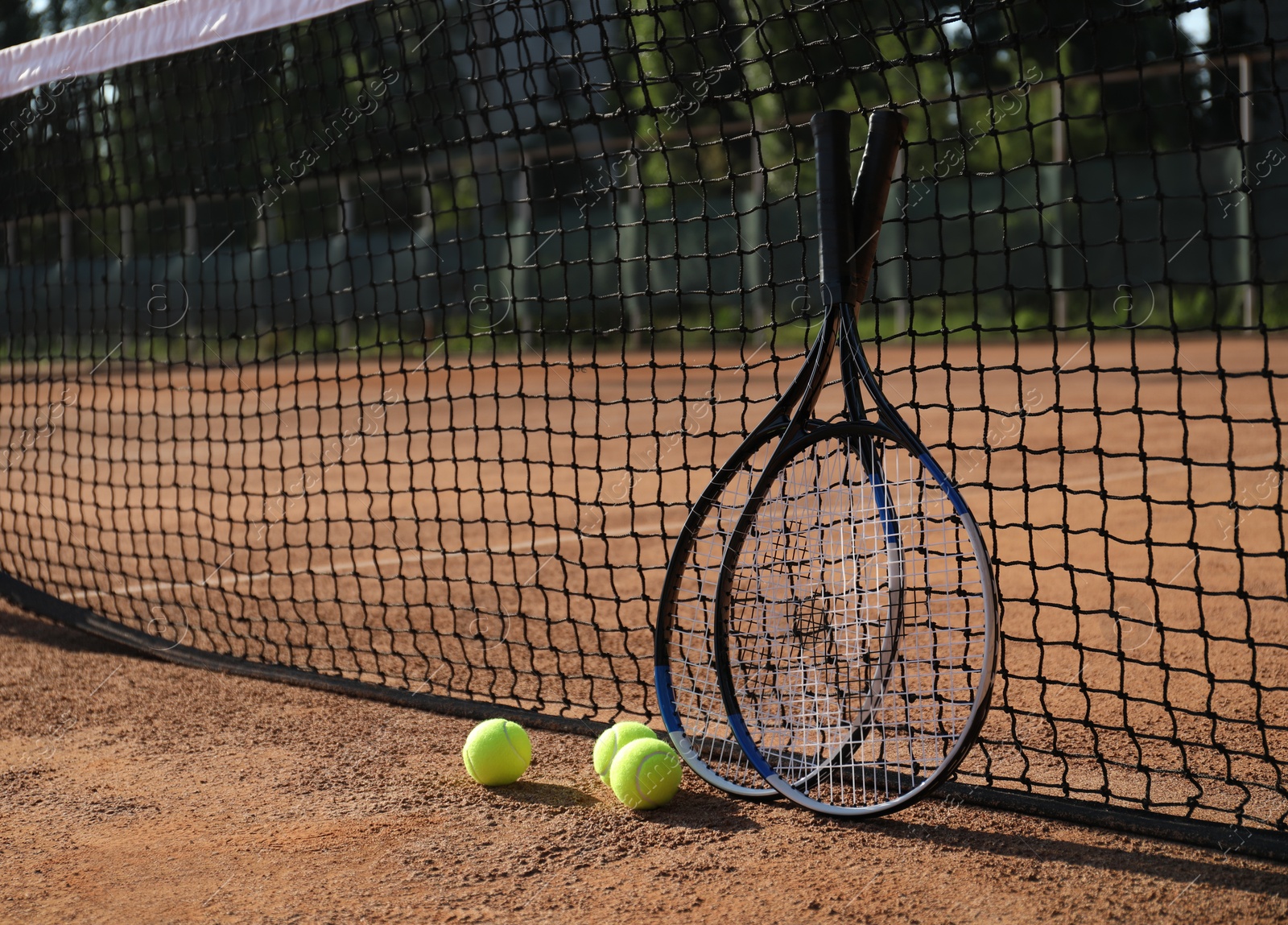 Photo of Tennis balls and rackets near net on clay court