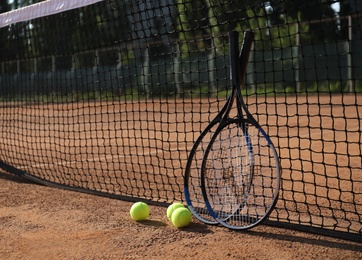 Photo of Tennis balls and rackets near net on clay court