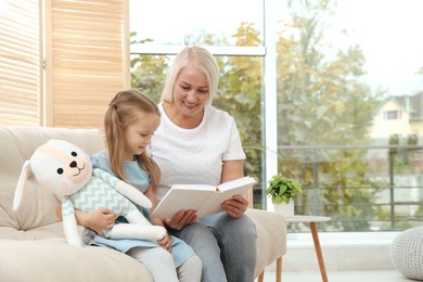 Happy grandmother with her granddaughter reading book together at home