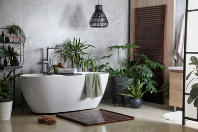 Photo of Modern white tub and beautiful green houseplants in bathroom. Interior design