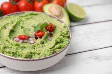 Bowl of delicious guacamole and ingredients on white wooden table, closeup. Space for text