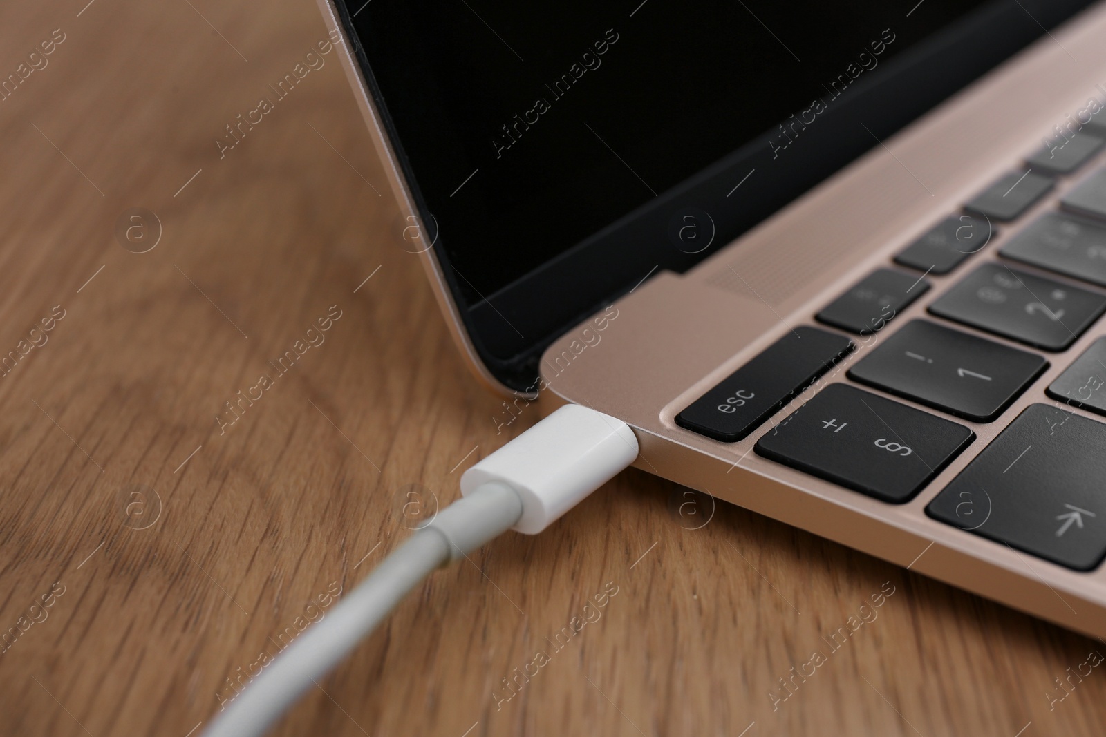 Photo of Modern laptop and charging cable on wooden table, closeup