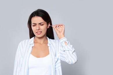 Young woman cleaning ear with cotton swab on light grey, space for text