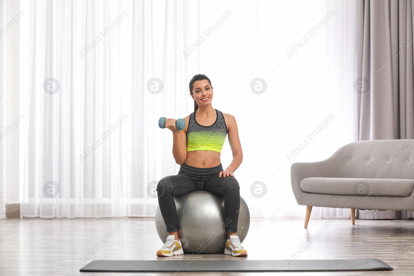 Photo of Young woman doing exercise with dumbbell on fitness ball at home