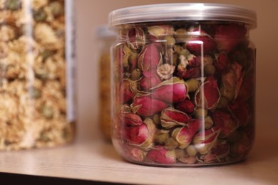 Glass jar with dry rose buds for tea on wooden shelf