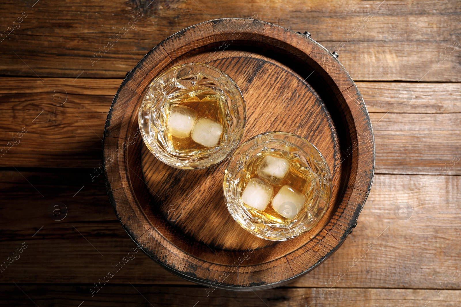 Photo of Glasses of whiskey and barrel on wooden background, top view
