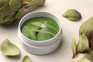 Photo of Package of under eye patches and artichokes on white table, closeup. Cosmetic product