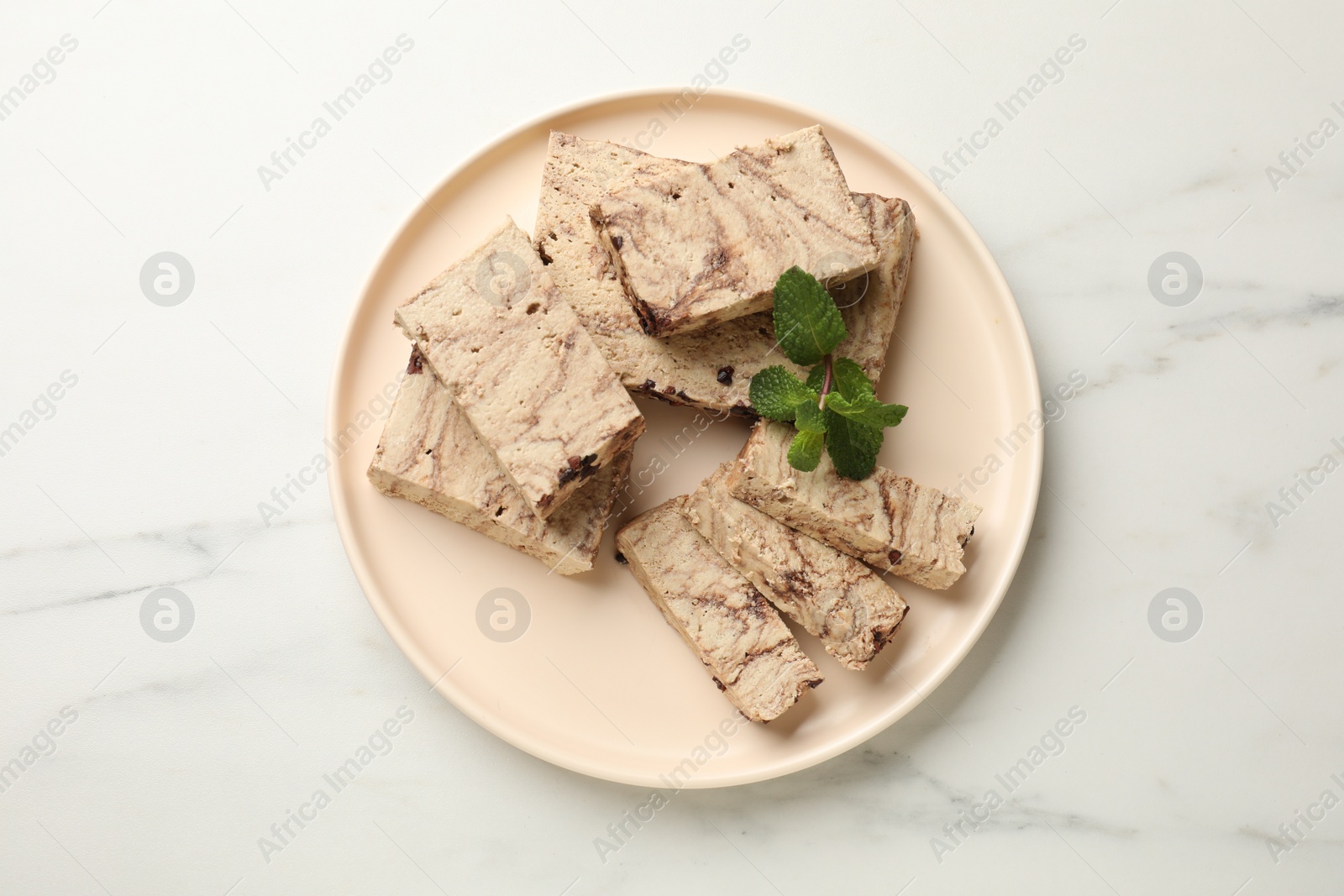 Photo of Pieces of tasty chocolate halva and mint on white marble table, top view