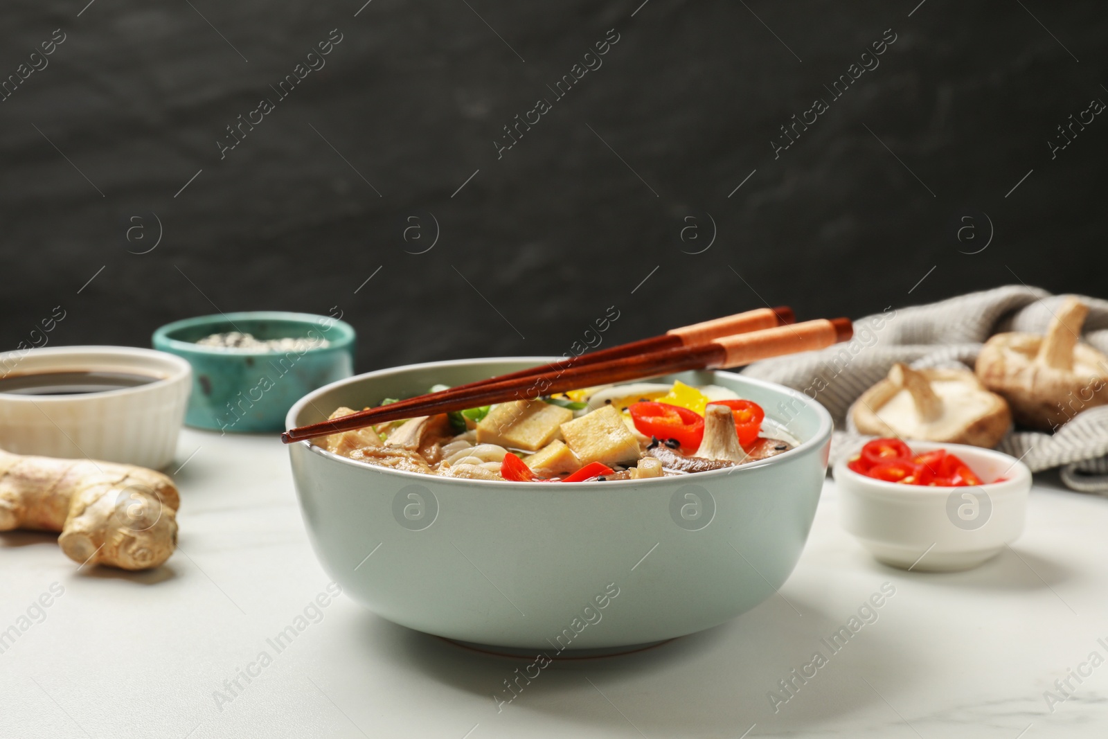 Photo of Bowl of delicious ramen, ingredients and chopsticks on white table, closeup. Noodle soup