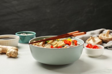 Photo of Bowl of delicious ramen, ingredients and chopsticks on white table, closeup. Noodle soup