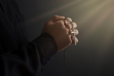Image of Holy light and priest with cross praying on black background, closeup