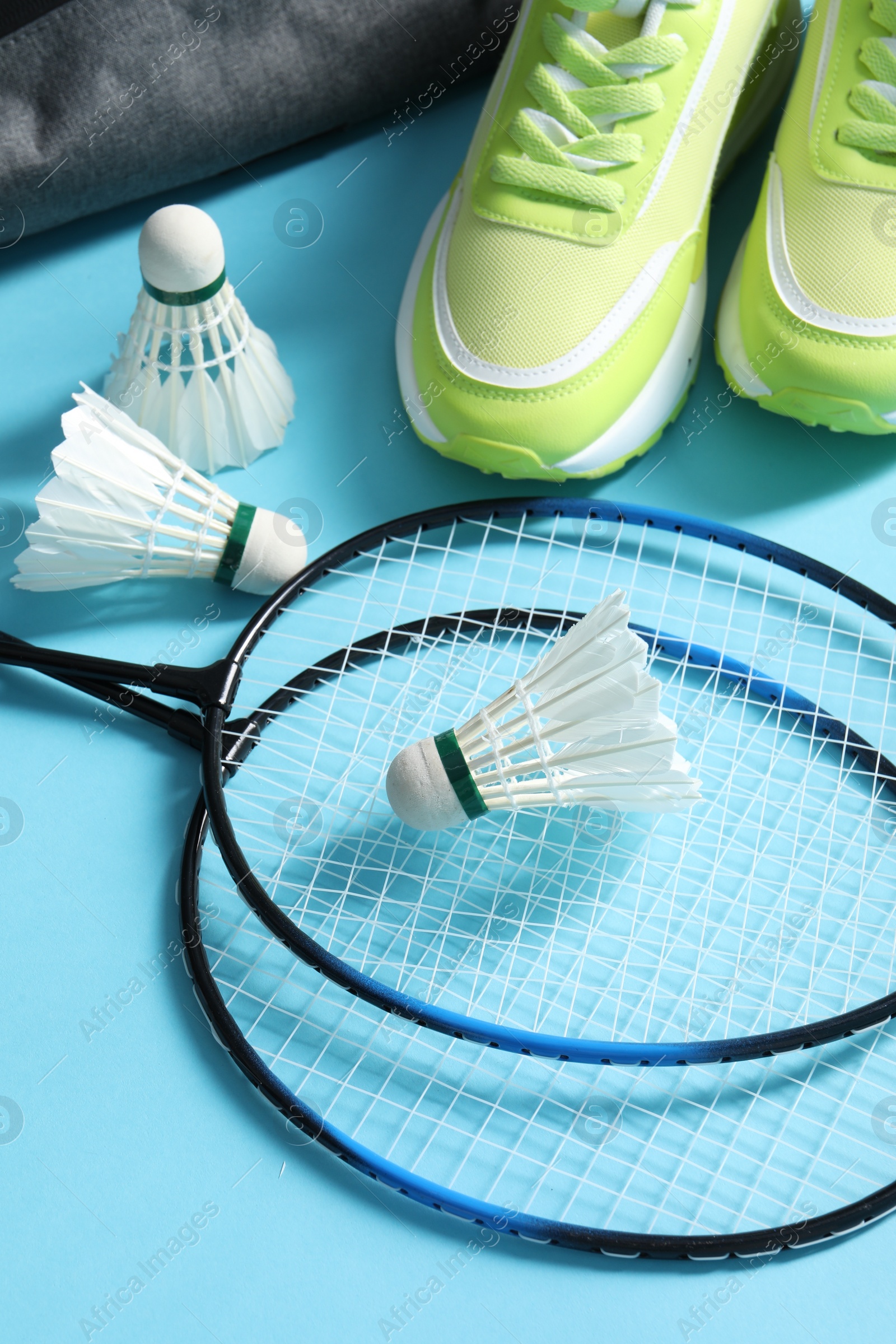 Photo of Feather badminton shuttlecocks, rackets and sneakers on light blue background