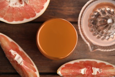 Photo of Glass of pink pomelo juice with squeezer and fruit on wooden table, flat lay