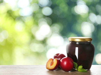 Jar of tasty pickled plums on wooden table against blurred green background. Space for text