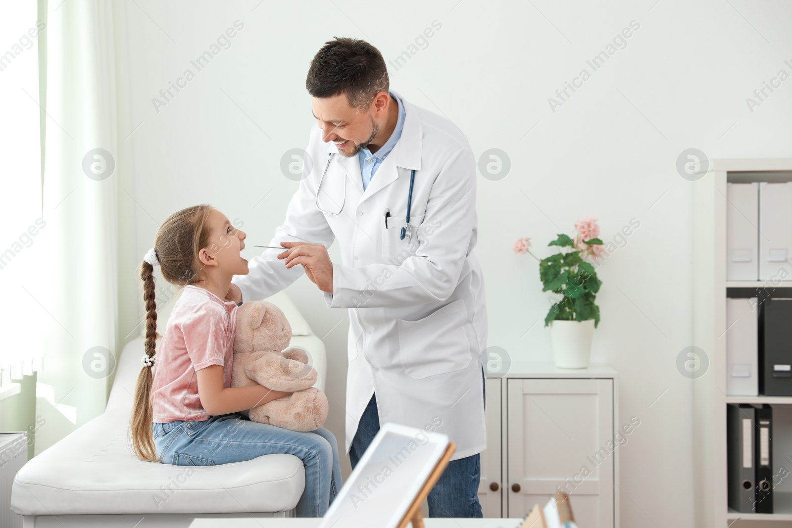 Photo of Children's doctor examining little patient's throat in clinic
