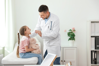 Photo of Children's doctor examining little patient's throat in clinic