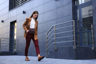 Young woman in formal clothes walking near building outdoors, space for text