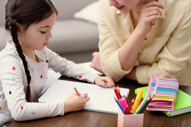 Photo of Woman helping her daughter with homework at table indoors