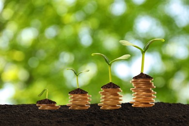 Image of Stacked coins and green seedlings on ground outdoors, bokeh effect. Investment concept