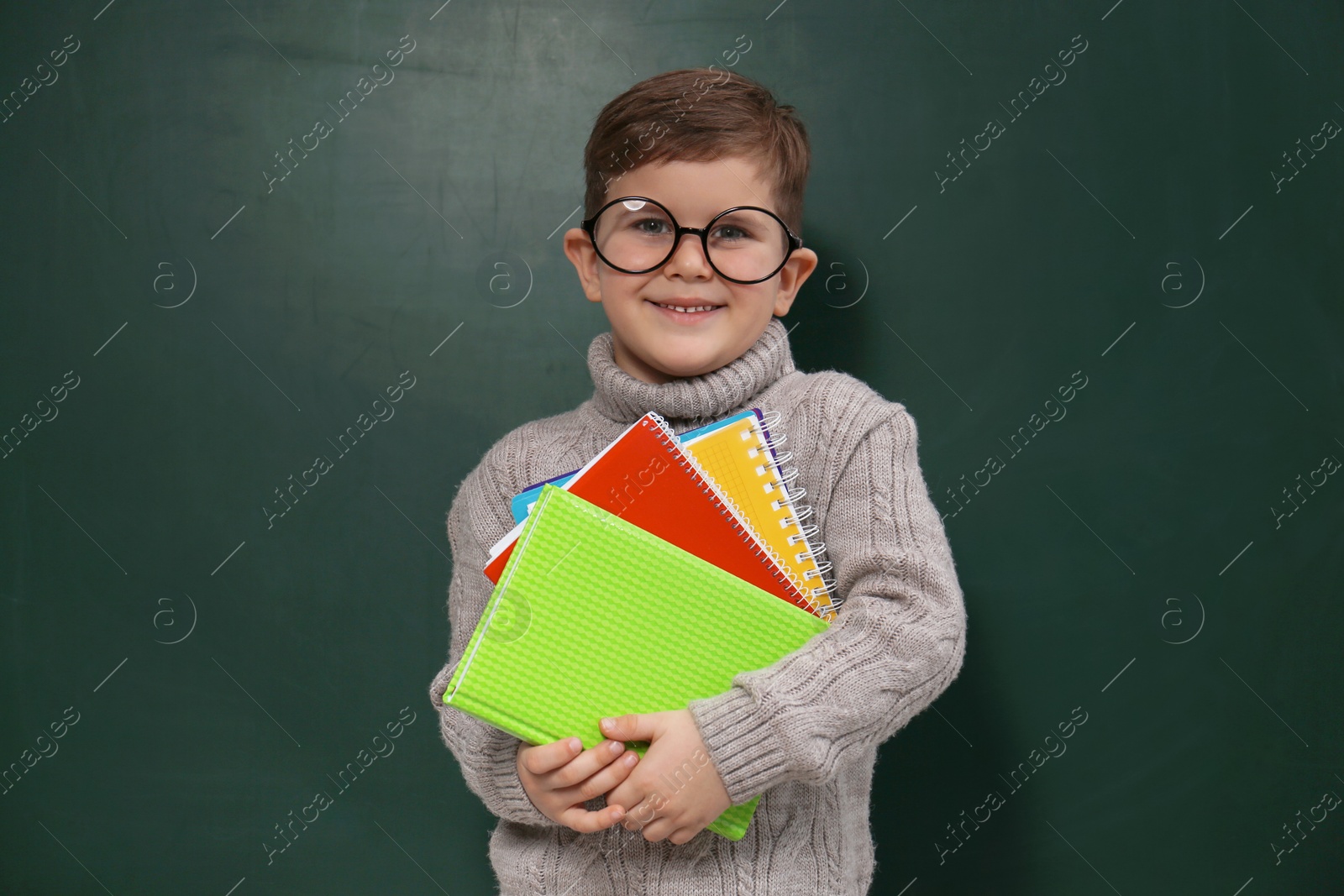 Photo of Cute little child wearing glasses near chalkboard. First time at school