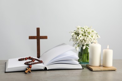 Church candles, Bible, wooden cross, rosary beads and flowers on grey table
