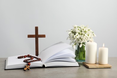 Photo of Church candles, Bible, wooden cross, rosary beads and flowers on grey table