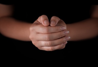 Photo of Woman holding hands clasped while praying against black background, closeup