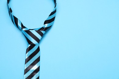 Photo of Striped necktie on light blue background, top view. Space for text
