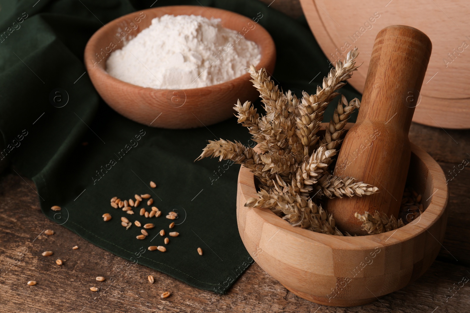 Photo of Mortar with spikes and bowl of wheat flour on wooden table, space for text