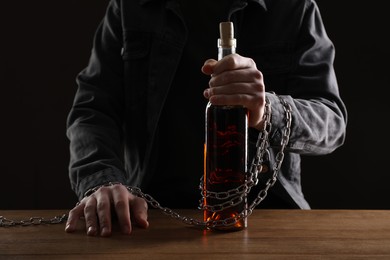 Photo of Alcohol addiction. Man chained with bottle of wine at wooden table, closeup