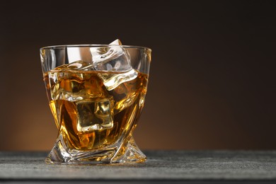 Photo of Whiskey and ice cubes in glass on grey textured table, closeup. Space for text