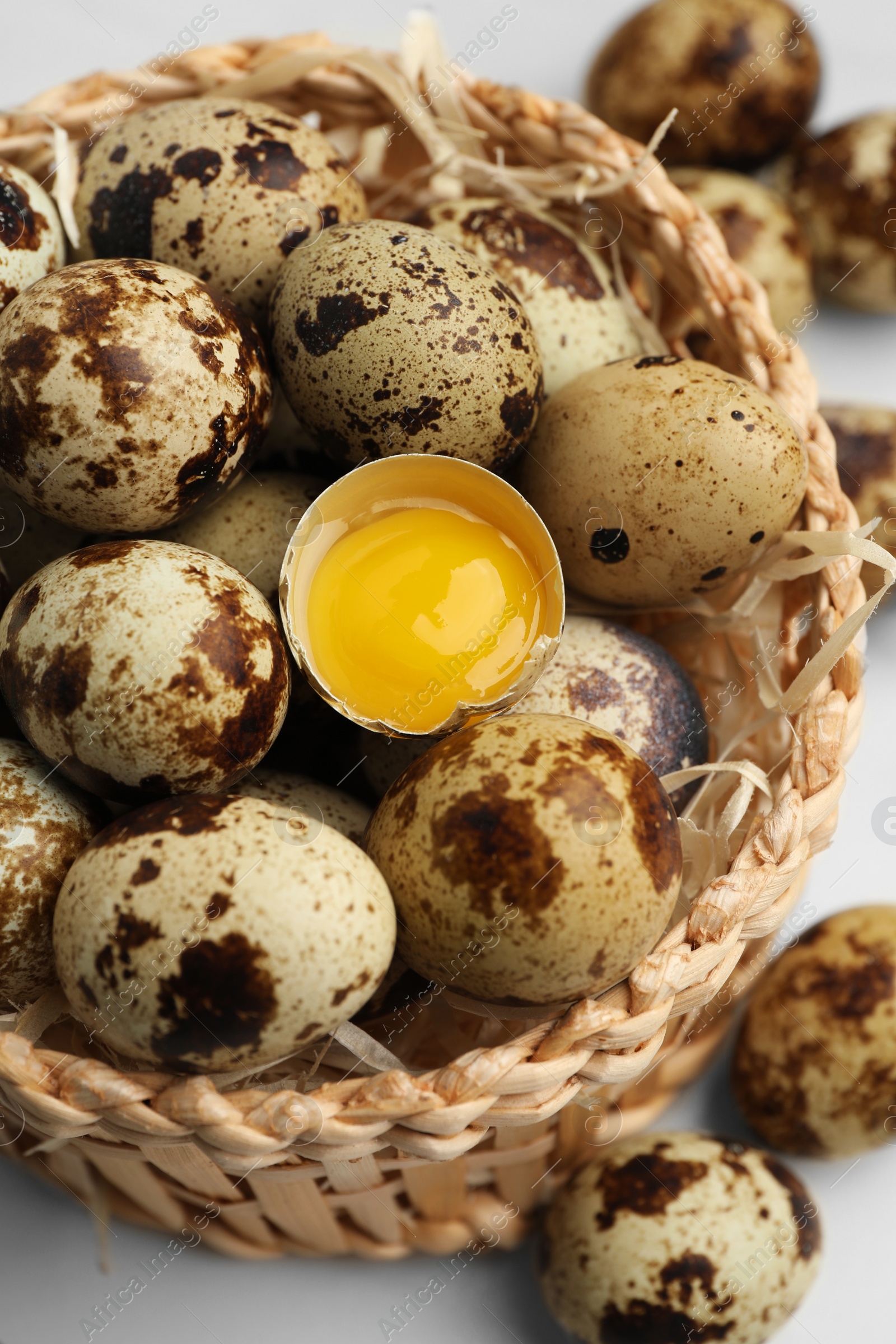 Photo of Wicker bowl with whole and cracked quail eggs on white table, closeup