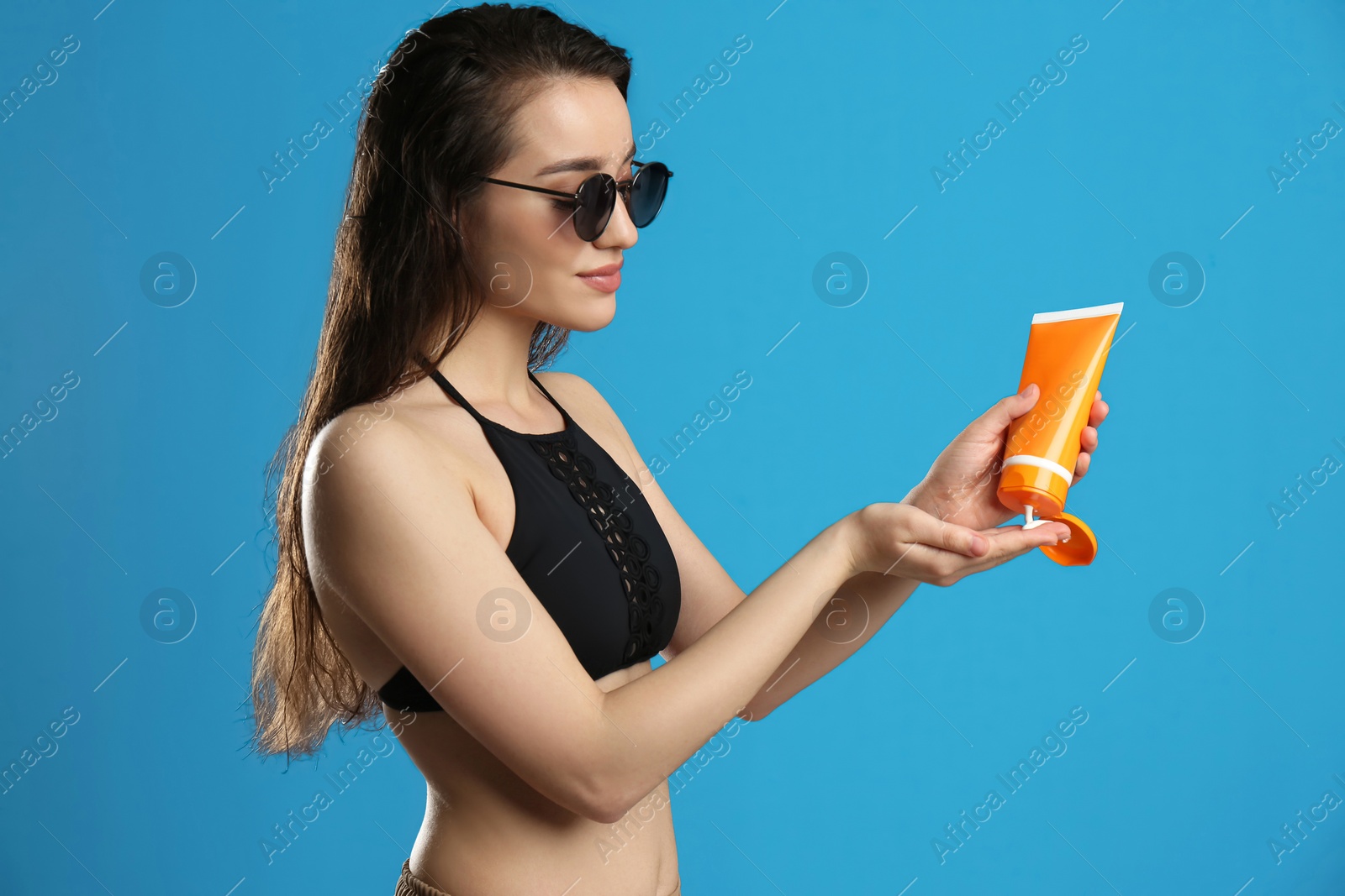 Photo of Young woman applying sun protection cream on blue background