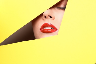 View of beautiful young woman with red lips through cutout in color paper, closeup