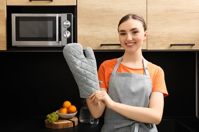 Photo of Beautiful young woman in clean apron and oven glove at kitchen