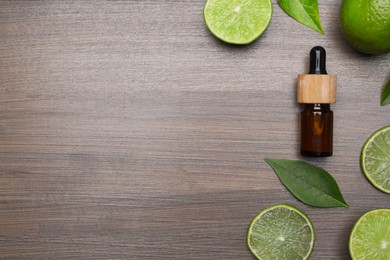Photo of Bottle of essential oil with lime slices and leaves on wooden table, flat lay. Space for text
