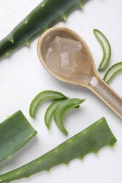 Aloe vera gel in spoon and slices of plant on white background, flat lay