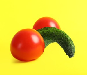 Cucumber and tomatoes symbolizing male sexual organs on yellow background. Potency problem