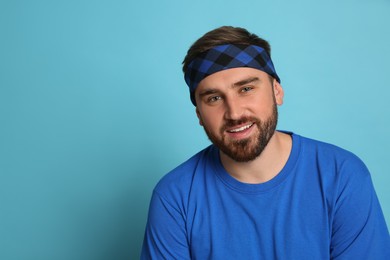 Fashionable young man wearing stylish bandana on light blue background, space for text
