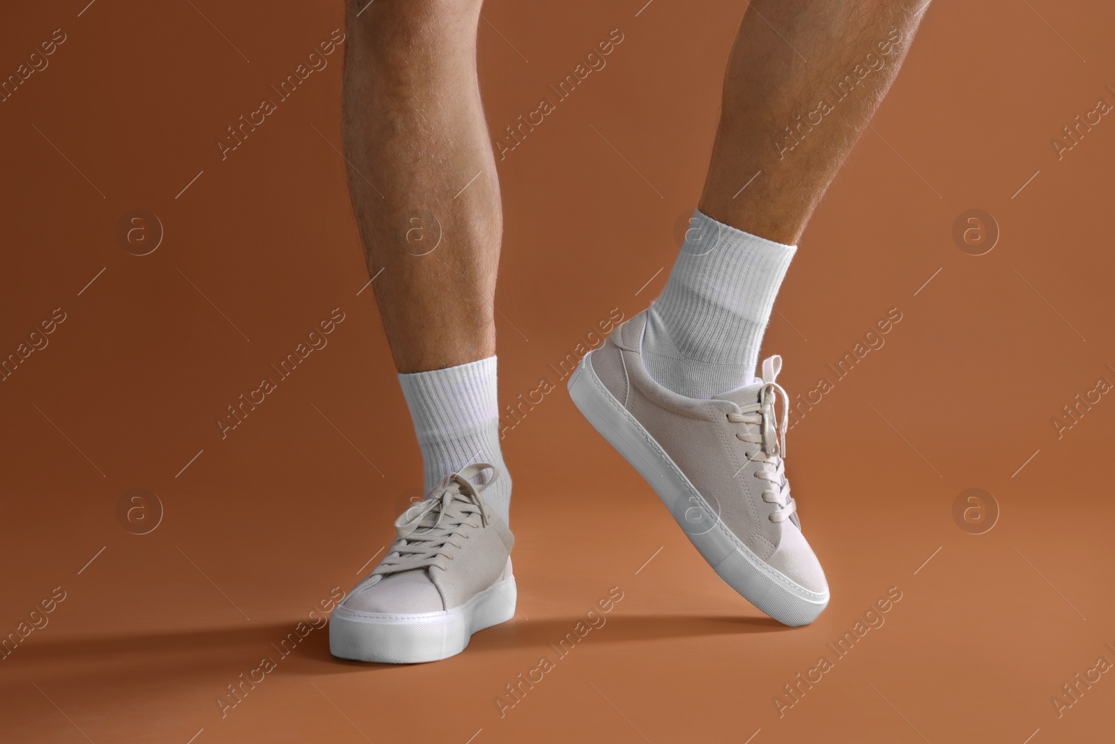 Photo of Man wearing stylish sneakers on brown background, closeup