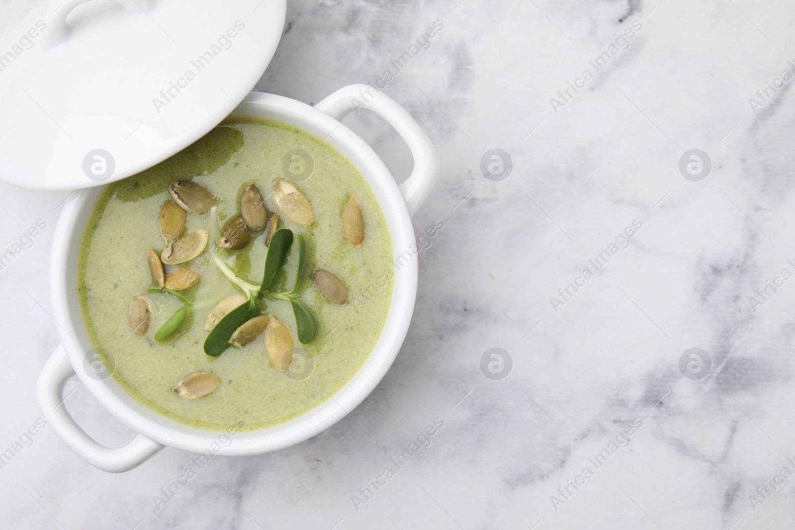 Photo of Delicious broccoli cream soup with pumpkin seeds on white marble table, top view. Space for text