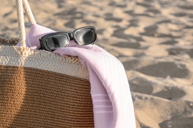 Photo of Stylish wicker bag, sunglasses and blanket on sand, closeup