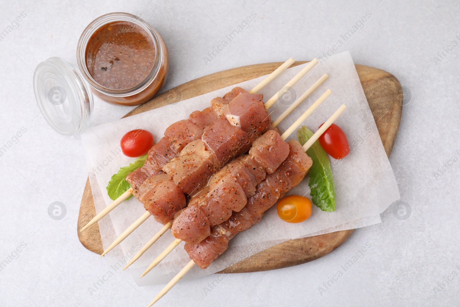 Photo of Wooden skewers with cut raw marinated meat on light grey table, flat lay